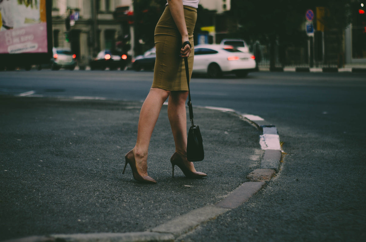 Femme en jupe camel et escarpins nude traversant la rue, sac noir à la main