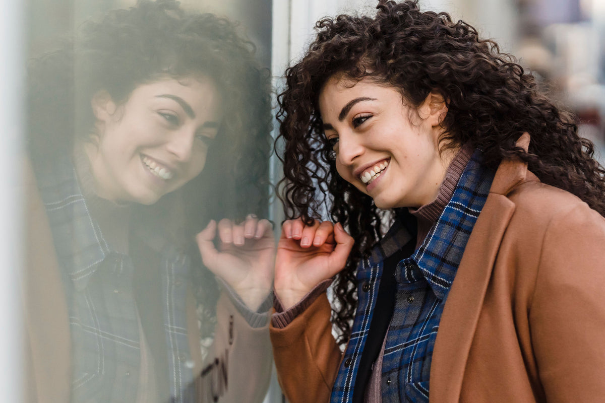 Femme souriante qui regarde son reflet dans une vitrine